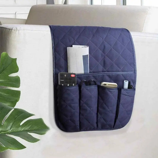 A navy blue sofa armrest organizer with multiple pockets, holding a remote control and other small items, placed on a sofa armrest.